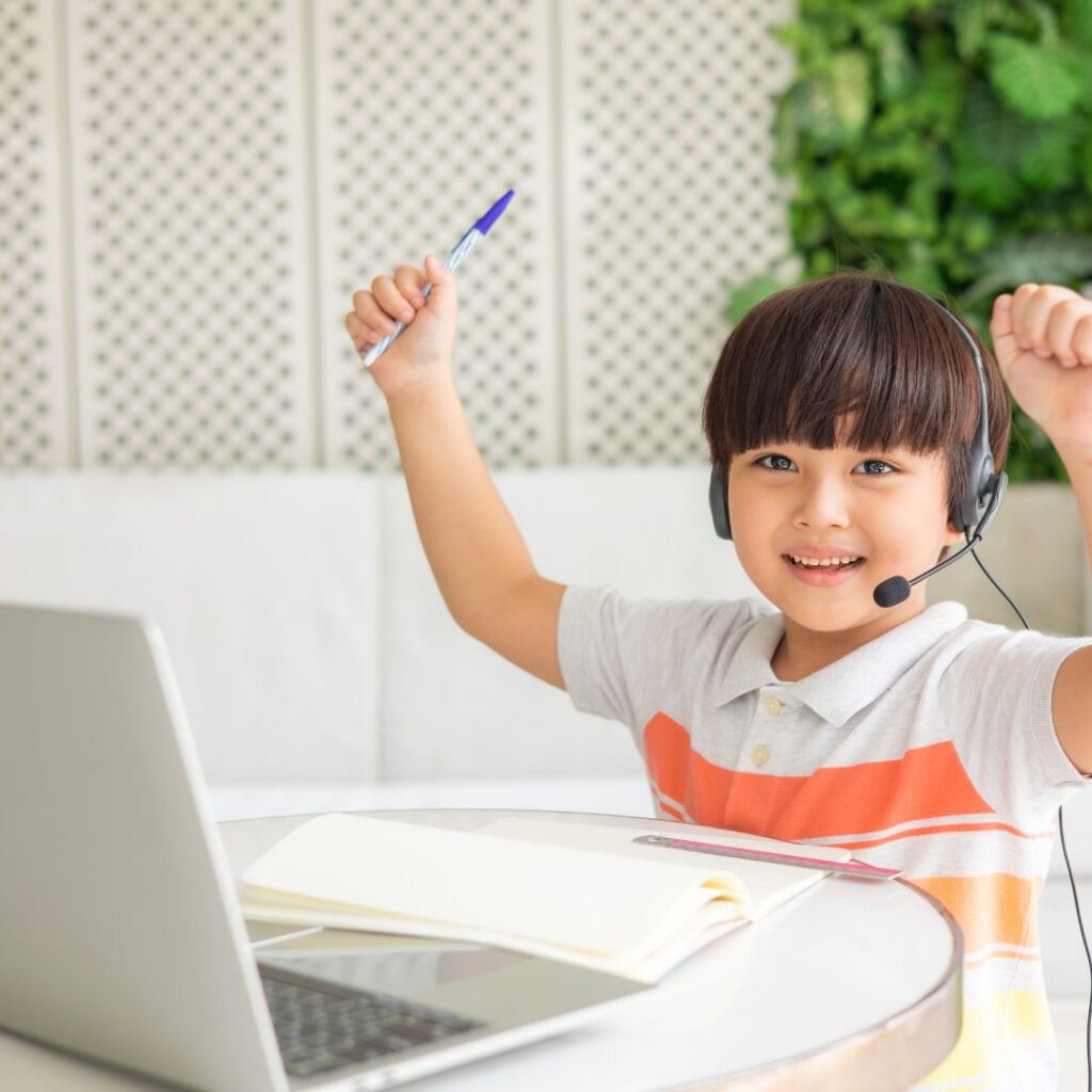 little boy raising hands in excitement while working on laptop